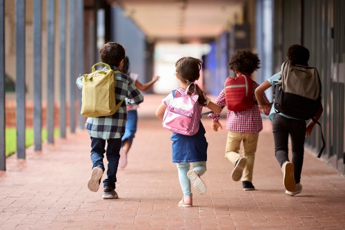 Group Of Multi-Cultural Elementary School Pupils Running Along Walkway Outdoors At School